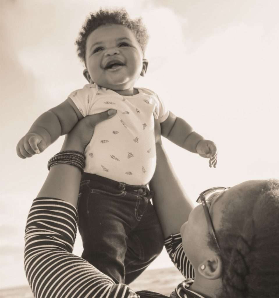 mother lifting delighted baby in the air. Photo by Lawrence Crayton