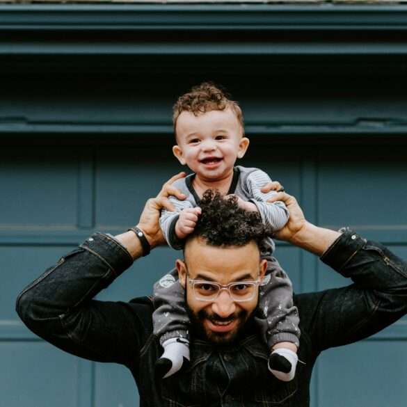 laughing baby sitting on smiling father's shoulders