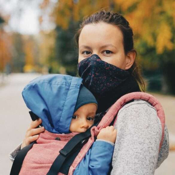 masked mother with child in baby carrier